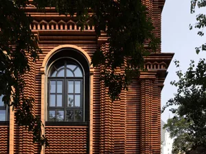 A modern building with a brick exterior, featuring a large arched window.