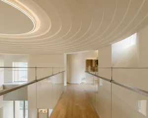 A modern corridor with a glass ceiling and wooden floor, featuring sleek railings and textured walls.