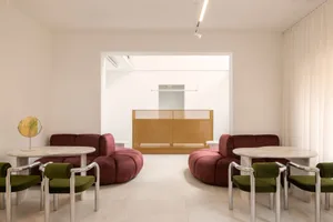 A minimalist living room featuring two round, red sofas, green chairs, marble tables, and a gold-toned divider.