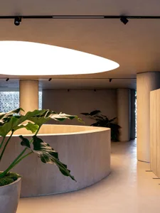 Modern office space featuring a sleek, curved reception desk made of concrete, illuminated by large, circular pendant lights.