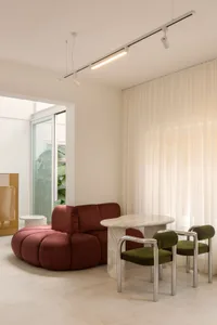 A modern living room featuring a soft, red, round sofa and a white marble table with green upholstered chairs.