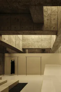 A minimalist clothing shop featuring black dresses hanging on racks with concrete walls and metal elements.