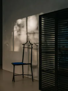 A minimalist interior with a metal chair casting a shadow on the wall.