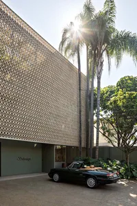 A modern exterior building with a patterned wooden facade and a classic black convertible car parked in front of it.