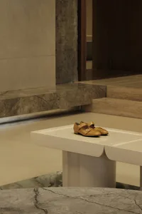 A minimalist shoe display made of white marble with a pair of mustard-colored shoes on top.