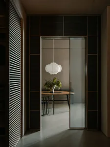 Modern minimalist dining room with a wooden table, a hanging pendant lamp, and a houseplant.