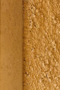 A close-up image showing a textured yellow plaster wall with a honeycomb pattern on the left side.