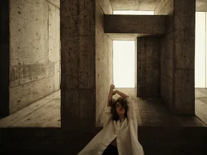 A young woman sitting on concrete walls with her arms raised.