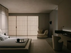 A minimalist bedroom with a bed, a round chair, a desk, and a large window with wooden blinds.