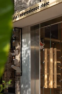 現代店面玻璃門，搭配木製把手與金屬框，背景為石牆與綠葉。
