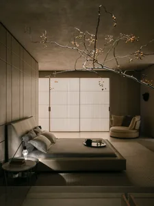 A minimalist bedroom with neutral tones and a low bed, featuring a side table with a light bulb and a tray with a teapot and