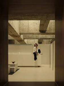 A woman sitting on a concrete wall in a modern interior space.