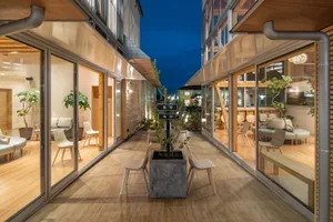 Modern building with a glass wall, wooden flooring, and a central seating area with chairs and a potted plant.