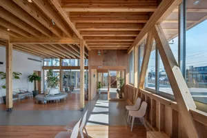 A modern office lobby featuring a wooden frame design with white waiting chairs and large windows allowing natural light to f