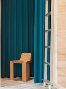 A minimalist wooden chair in front of a blue curtain.