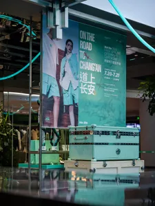 零售店面展示大型藍綠色行李箱，並有文字宣傳線下開幕典禮活動。