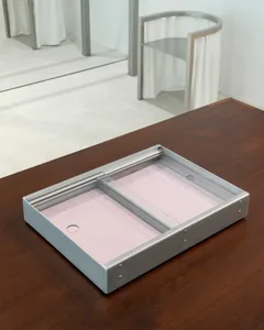 A metal rectangular product bin with pink sheets inside, placed on a wooden table.