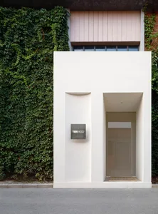 A modern, minimalist building exterior made of concrete, with green ivy covering one side.