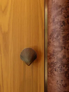 A modern interior design featuring a wooden door with a brass scallop-shaped handle.