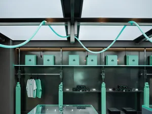A modern storefront with green lighting and mixed materials, featuring shelves with boxes and clothing items.