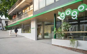 A modern retail storefront featuring glass windows, concrete walls, and greenery.