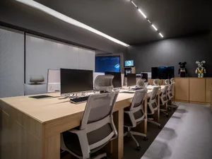 A modern, minimalist workspace desk setup with white chairs, desks, and computers.