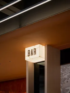 An illuminated metal sign displaying the word 'BAR' in a minimalist, industrial interior setting.