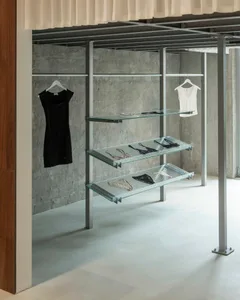 極簡服裝展示，以黑白服飾陳列於金屬衣架及內嵌玻璃的層架上。