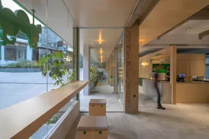 A modern coffee shop with concrete interior, featuring a large window displaying plants outside.