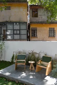 An outdoor seating area with modern furniture featuring wooden frames and green cushions, situated against a white wall with 