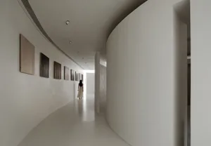A minimalist corridor with white plaster walls and a curved entrance to a room.