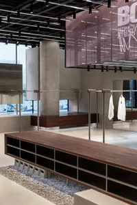 A modern retail space featuring clothing racks, concrete floors, metallic accents, and glass dividers.