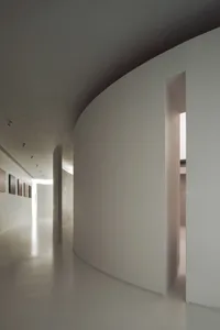 A minimalist interior space featuring a concrete corridor with white walls and a curved wall.