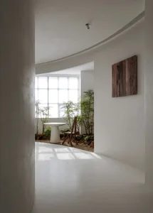 A minimalist white interior with curved space, featuring modern furniture and plants in a small garden.