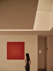 A woman stands in a minimalist bedroom with a large red square painting on the wall and beige walls