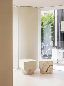 A modern retail interior features a minimalist design with wooden blocks for seating and a window showcasing the exterior vie