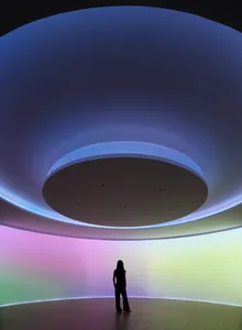 A person standing in a room with a circular light installation featuring LED lighting in shades of purple, blue, and green.