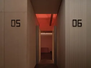 A minimalist industrial-style interior corridor with concrete walls, corrugated metal columns, and a red-tinted ceiling.
