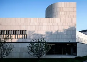 A minimalist building exterior made of granite blocks, featuring a curved facade and large windows.