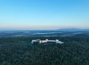 A modern building nestled in a forested area with clear blue sky and distant mountains.