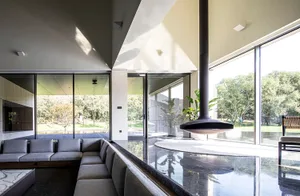 Modern living room with floor-to-ceiling glass windows, concrete walls, and a steel fireplace.