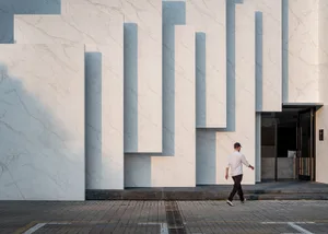 A man walking in front of a modern storefront with a marble facade.