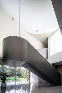 A modern, minimalist staircase made of black metal, featuring curved steps in a spacious, light-filled interior.