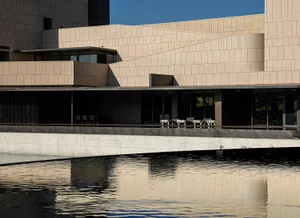 A modern public building with concrete and glass surfaces reflected in water.