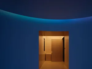 A minimalist corridor featuring glass walls, concrete flooring, and wooden elements with blue lighting.