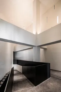 A contemporary interior space featuring a black cube structure and concrete walls and floor.