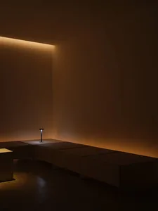 A minimalist interior space with a concrete bench and a small table lamp.