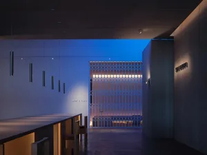 A minimalist bar featuring wooden stools, metal ceiling lights, and a wooden wall with a grid design.