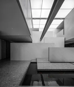 Modern interior design featuring a minimalist lobby with concrete and glass materials, illuminated by overhead lighting.