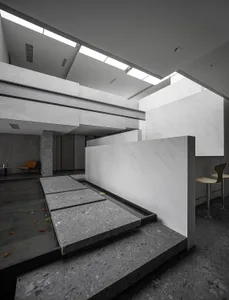 A modern lobby featuring marble and concrete walls, with a water feature and seating areas.